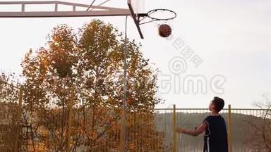 体育和<strong>篮球</strong>。 一个穿着蓝色运动服的青少年领着球，然后把球扔进篮子。 天空和树林